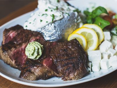 Zu sehen ist ein Beefsteak, serviert mit Folienkartoffel und Kräutersoße.